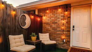 A patio with two chairs, a small table, a potted plant, a wooden fence, and a brick wall. - FIFA26 Chic Suite - Near NRG  (Houston)