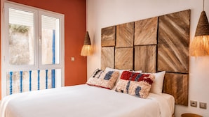 A bedroom with a large bed, a wooden headboard, two wall-mounted lamps, and a small wooden table. - Waterfront Apartment - Ocean View (Essaouira)