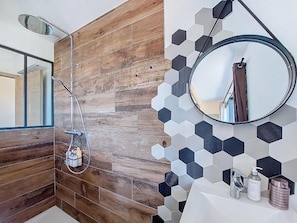 Ein Badezimmer mit Holzwand, einer Dusche, einem Spiegel und einem Waschbecken mit Pflegeprodukten.