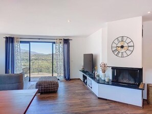 Ein modernes Wohnzimmer mit Kamin, einer großen Wanduhr und Blick durch eine Glastür.