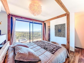 Ein Schlafzimmer mit einem großen Bett, Blick durch eine Schiebetür, einer Deckenleuchte und einem an der Wand befestigten Kunstwerk.