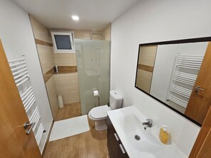 A compact bathroom with a toilet, sink, and glass shower enclosure. - Grandfather's House (Santana)