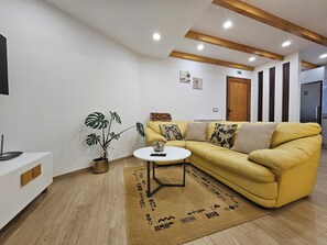 A modern living room with a yellow sofa, a round coffee table, a potted plant, and a wooden floor. - Grandfather's House (Santana)
