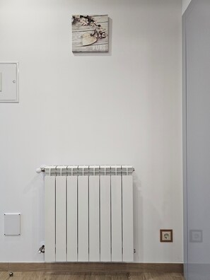 A room with a white radiator, a wooden floor, and a wall-mounted light switch. - Grandfather's House (Santana)