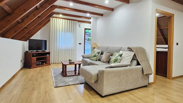 A living room with a sofa, a TV on a stand, a small table, and a wooden ceiling. - Grandfather's House (Santana)