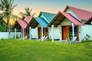 Una hilera de alojamientos tipo bungalow con techos individuales, un césped bien cuidado y un paisaje tropical de fondo.
