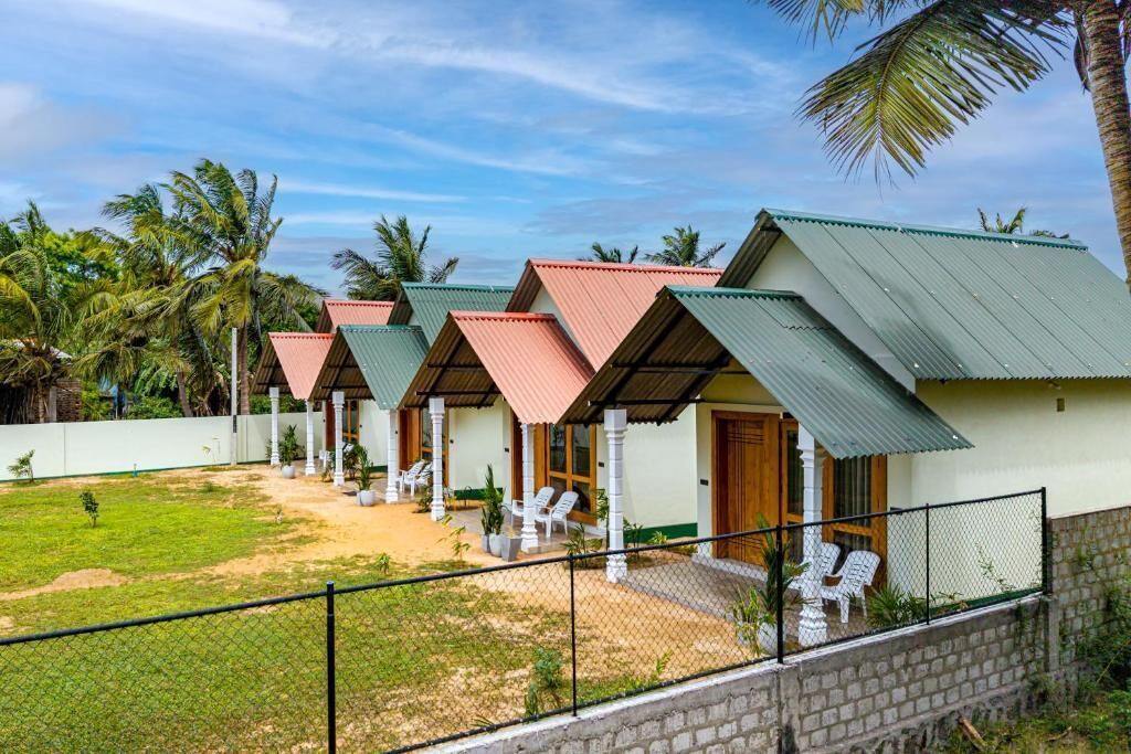 Eine Reihe von Bungalows mit Satteldächern, ein eingezäunter Außenbereich mit Stühlen und Palmen im Hintergrund.