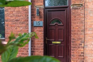 A brick building with a dark wooden door, a number plate with '15', and a small window above the door. - Perfect Home for Trades or Small Families (Greater Manchester)