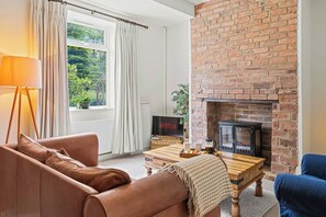 A living room with a brick fireplace, a sofa, a coffee table, and a TV displaying Netflix. - Perfect Home for Trades or Small Families (Greater Manchester)