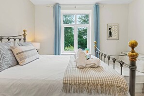 A neatly made bed with a checkered throw blanket, a bedside table with a lamp, and a window with curtains. - Perfect Home for Trades or Small Families (Greater Manchester)