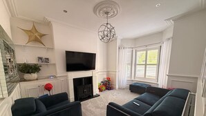 A living room with dark blue sofas, a flat-screen TV, a fireplace, and a large window with white curtains. - Contractor, Families, Free Parking, Private Garden (Worsley)