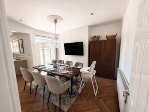 Ein Essbereich mit einem Holztisch, Stühlen und einem an der Wand befestigten Fernseher.