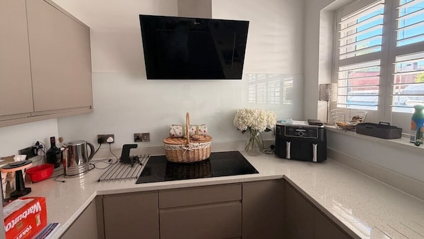 A modern kitchen with a flat-screen TV, a built-in oven, and a window with blinds. - Contractor, Families, Free Parking, Private Garden (Worsley)