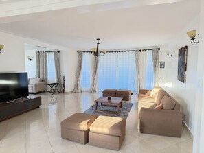 Ein modernes Wohnzimmer mit Flachbildfernseher, Sofas, Poufs und einem Chandelier.