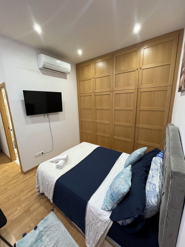 Un dormitorio con cama, televisor montado en la pared, armario de madera y equipo de aire acondicionado.