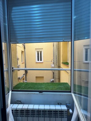 Una ventana con vistas al exterior de un edificio, una ventana pequeña y un radiador.