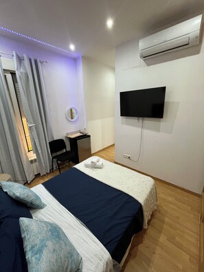 Habitación de hotel con cama, escritorio, silla, televisión y aire acondicionado.