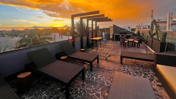 Eine Dachterrasse mit Außenbestuhlung, einem Grill und Blick auf den Sonnenuntergang.