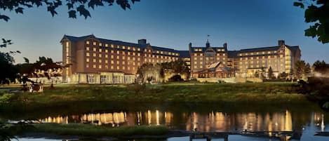 A large hotel with multiple floors, a reflective pond in front, and a well-maintained lawn.
