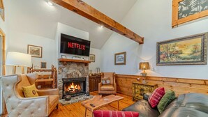 A cozy living room with a fireplace, leather sofa, wooden coffee table, and a Netflix TV mounted above the fireplace. - Heart of Helen Cabin (Helen)