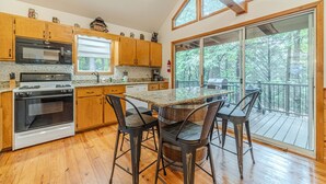 A kitchen with wooden cabinets, a microwave, an oven, a dining table with chairs, and a large sliding glass door leading to a deck. - Heart of Helen Cabin (Helen)