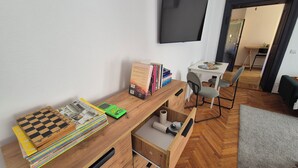 Une pièce avec un bureau en bois, des livres, un téléviseur à écran plat, une petite table avec des chaises et un parquet à motifs en chevrons.