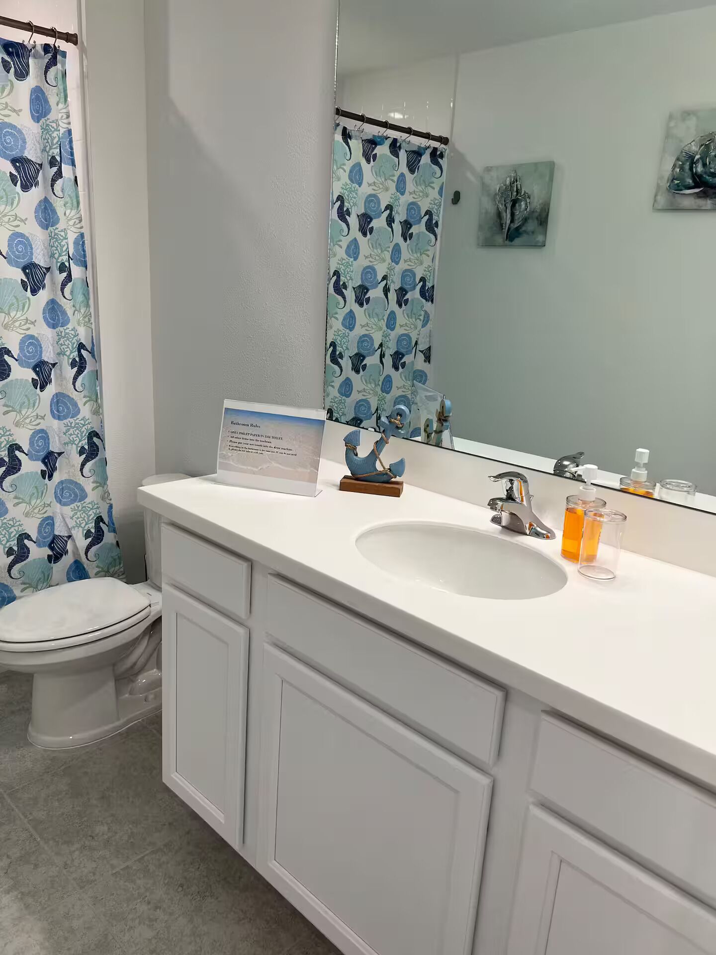 Un baño con lavamanos blanco, un espejo, un inodoro y una cortina de ducha con estampado azul y verde.