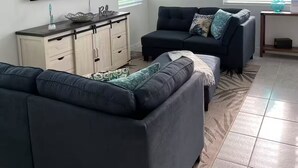 Ett vardagsrum med en takfläkt, en platt-TV, en soffa i mörk färg, ett soffbord och ett skåp med lådor.