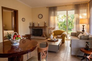 A living room with a fireplace, a dining table with a fruit bowl, a sofa, and a coffee table.