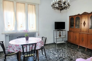 Zona pranzo con tavolo rotondo, sedie, una pianta in vaso, televisore su un mobile e un armadietto in legno.
