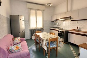 Een kleine keuken met een eettafel, een koelkast, een fornuis en een raam met gordijnen.