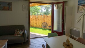 A room with a sofa, a dining table, and a view of a fenced backyard. - Villa Patio Léon & Gustave - Quiet & walking distance (Vieux-Boucau-les-Bains)