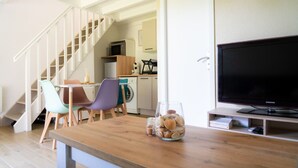 A compact living space with a wooden dining table, chairs, a TV, a kitchen area with a microwave, and a staircase. - Villa Patio Léon & Gustave - Quiet & walking distance (Vieux-Boucau-les-Bains)