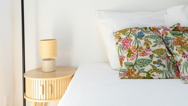 A bed with white bedding and a floral pillow, a bedside lamp on a wooden nightstand, and a plain wall. - Villa Patio Léon & Gustave - Quiet & walking distance (Vieux-Boucau-les-Bains)