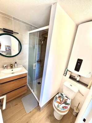 Une salle de bain moderne avec une douche Ă lâitalienne en verre, des toilettes ornĂ©es de motifs floraux colorĂ©s et un lavabo avec un miroir.