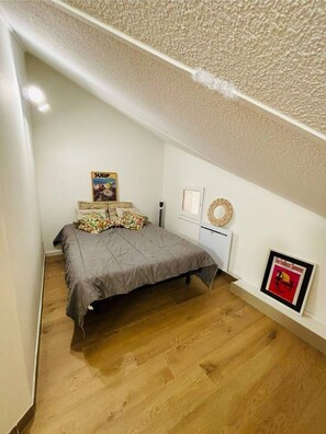 Une chambre à coucher comprenant un lit, un radiateur fixé au mur, une affiche encadrée et une petite étagÚre sur laquelle est posé un objet décoratif.