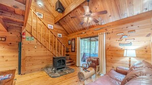 A cabin interior with a wooden staircase, a fireplace, leather seating, and a ceiling fan. - Unicoi Pines | Hot Tub, Pet-Friendly Cabin Near Helen, GA (Sautee Nacoochee)