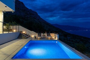 A swimming pool with steps leading up to it, surrounded by a modern building with outdoor seating and a view of the mountains. - Seaview Villa EBS, Your Mediterranean Retreat (Lokva Rogoznica)