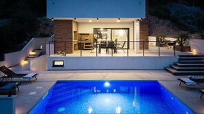 A modern house with a swimming pool, outdoor seating, and a kitchen visible through glass doors. - Seaview Villa EBS, Your Mediterranean Retreat (Lokva Rogoznica)