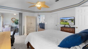 Ein Schlafzimmer mit einem Bett, einem Fernseher, einem Deckenventilator, einer Kommode und einem Schreibtisch.