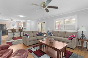 Ein Wohnzimmer mit einer Couch, einem Couchtisch, einem roten Ledersessel, einem Deckenventilator und einer Küche im Hintergrund.