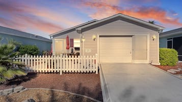 A single-story house with a garage, a white picket fence, and a driveway leading to the garage.