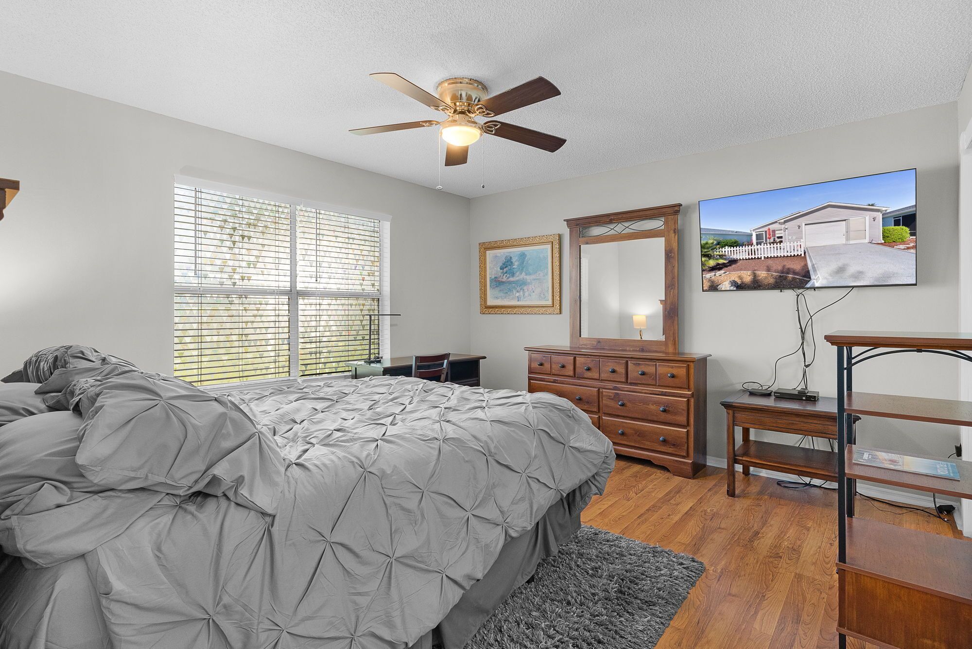 Une chambre à coucher comprenant un lit, une commode, une coiffeuse et un ventilateur de plafond.