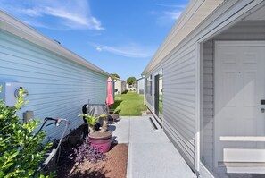 A narrow pathway leading to a row of mobile homes with a small garden area and a door on the right.