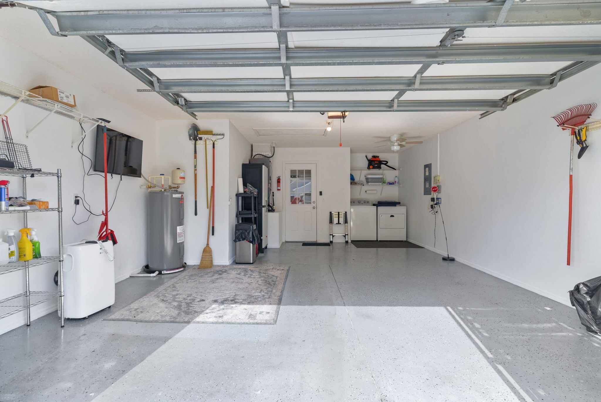 A garage with a concrete floor, a white refrigerator, a broom, a vacuum cleaner, and a ceiling fan.