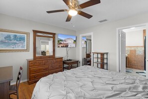 A bedroom with a bed, dresser, ceiling fan, and a painting on the wall.