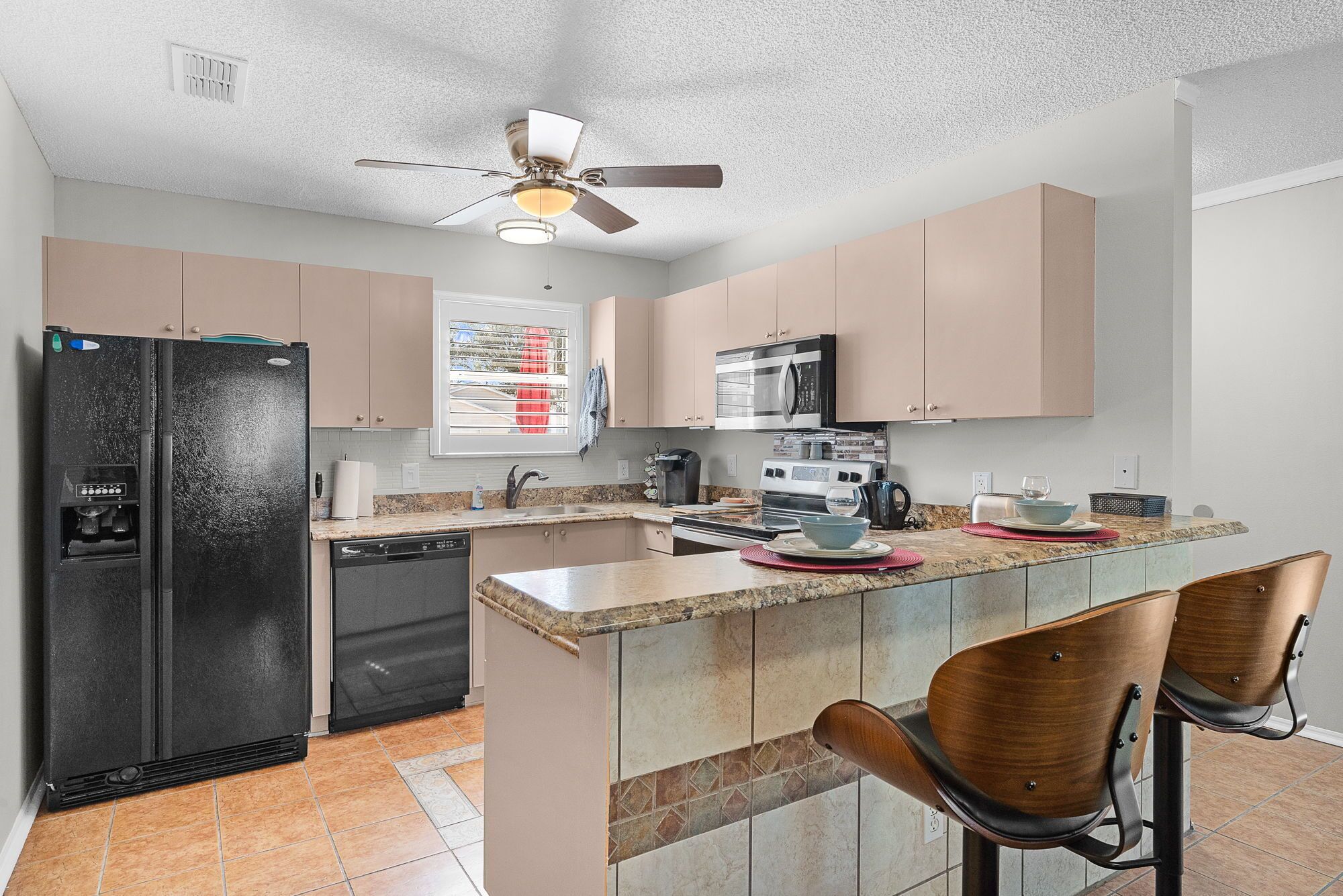 A kitchen with a refrigerator, microwave, stove, and a ceiling fan.
