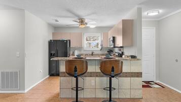 A kitchen with two bar stools, a ceiling fan, and a refrigerator.