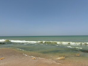 Ein Strand mit klarem Wasser, sandigem Ufer und blauem Himmel.