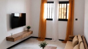 Un soggiorno moderno con televisore a schermo piatto, mobile in legno, divano e tavolino con una pianta.